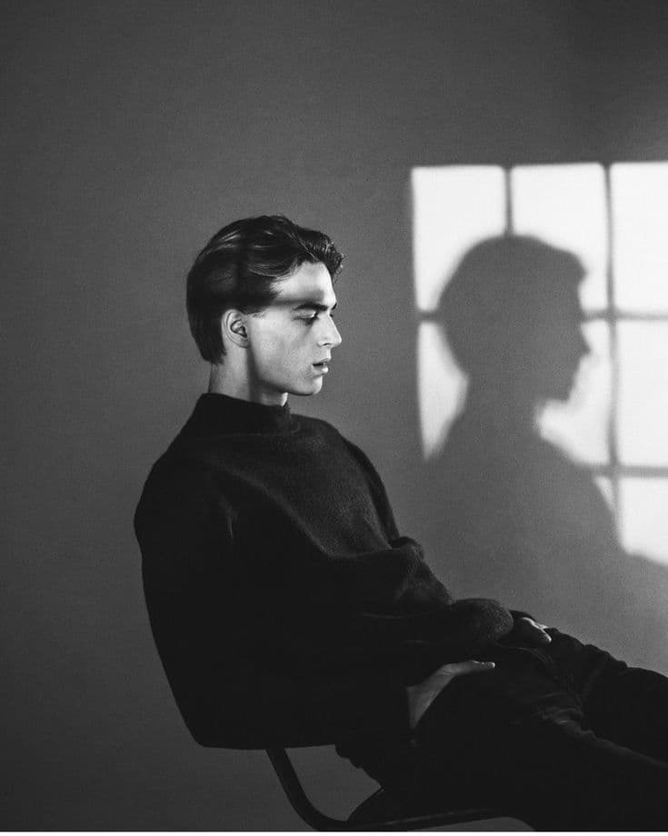 Black-and-white portrait of a person seated in profile, with a window's shadow on the wall