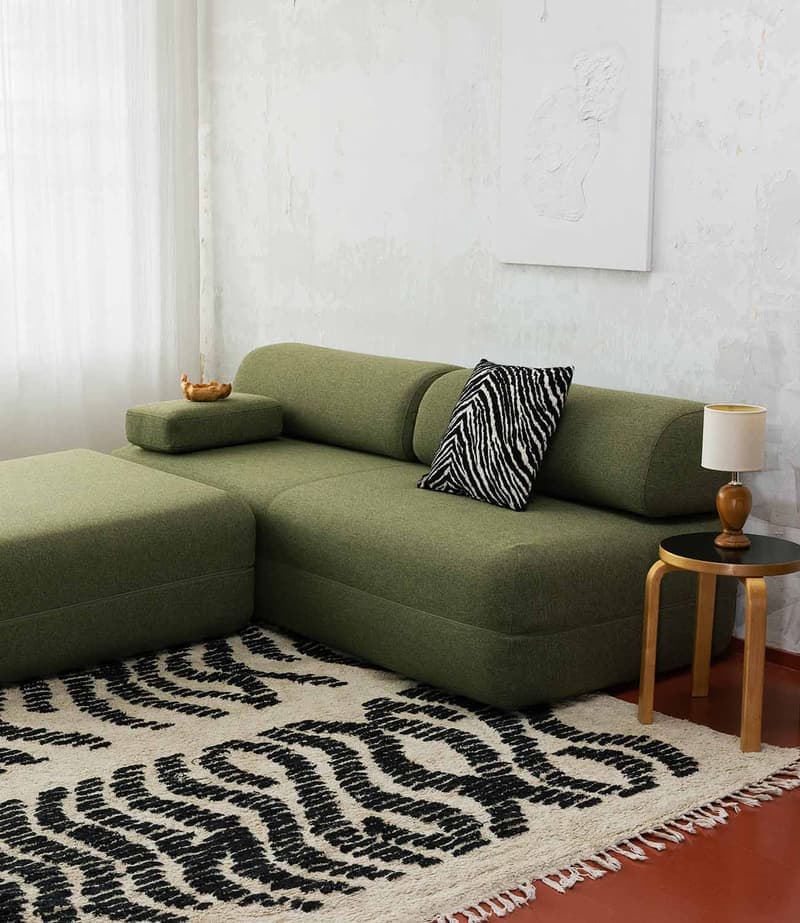 KHOY: a green modular sofa with a zebra-pattern cushion on a black and cream rug, beside a wooden stool with a table lamp